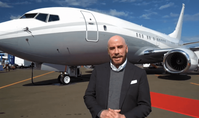 John Travolta talking to the camera in front of an airplane, Photo Credit: johntravolta/Instagram